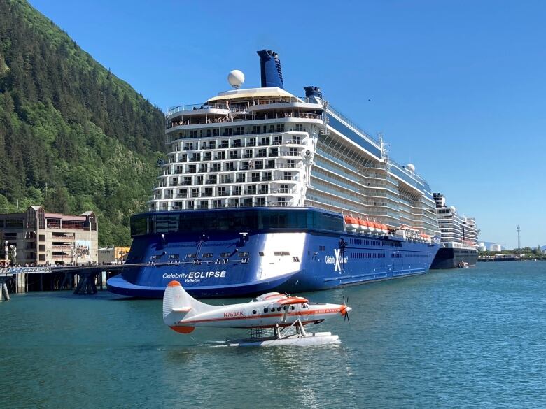 A float plane is seen on the water in front of a large, docked cruise ship 