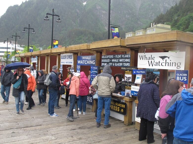 People stand about by a row of kiosks on a wooden boardwalk.