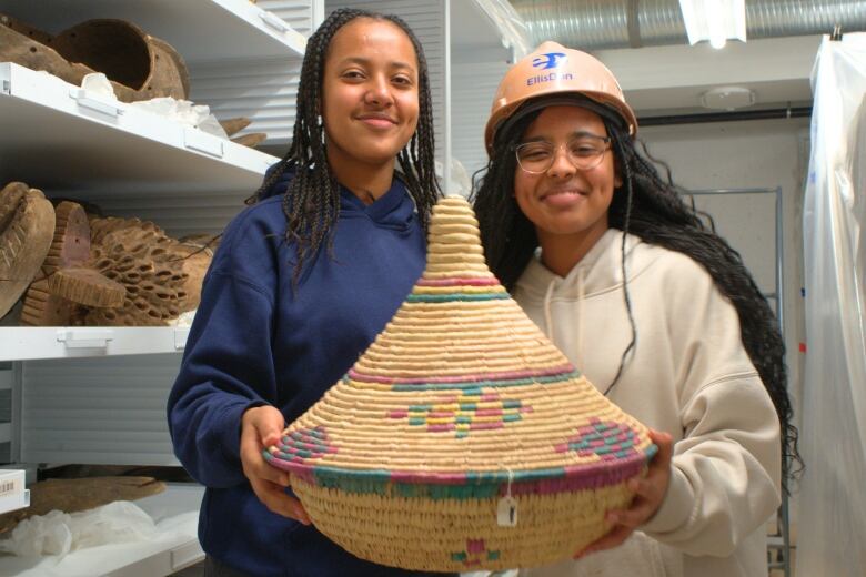 Two students with roots in Ethiopia hold up a traditional basket made of grass. 