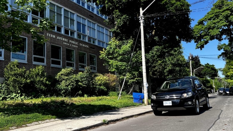 A black car passes by a public school. 