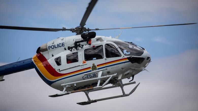 A helicopter with RCMP regalia, including a logo, is pictured in the sky.