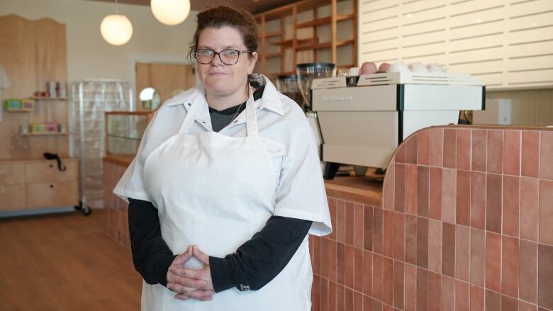 A woman wearing a white apron stands in front of a counter