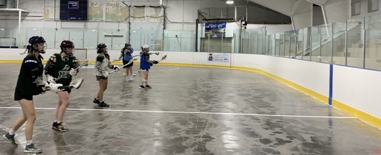 A line of lacrosse players doing practicing drills throwing balls against arena wall.