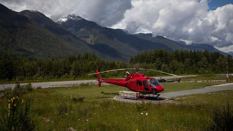 A red helicopter on a helipad with mountains in the background. 