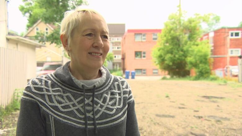 A woman with short grey hair is standing in front of a vacant lot.