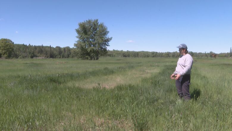 A woman sporting a cap is seen standing on a large patch of grass.