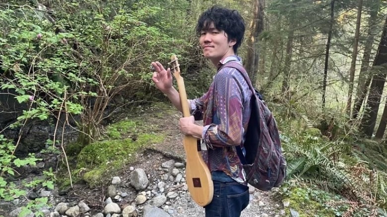 a portrait of a man carrying a guitar in the forest