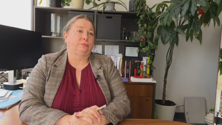 A woman sits at a desk with her hands crossed looking at the camera.