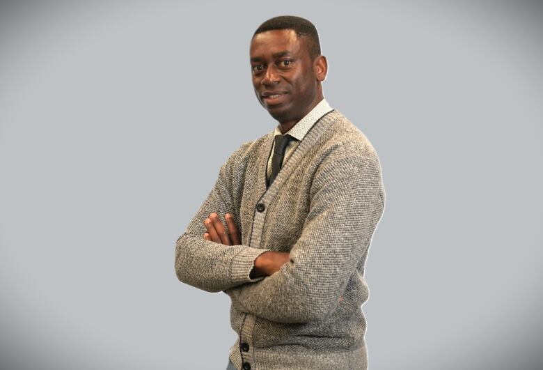 A man with Winnipeg a white collared shirt and grey cardigan crosses his arm in a pose.