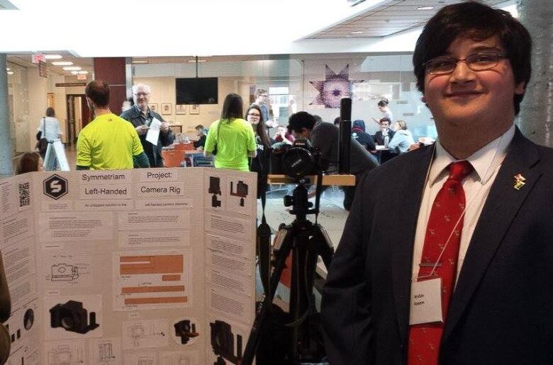 A youth stands by his project in a suit at a convention 