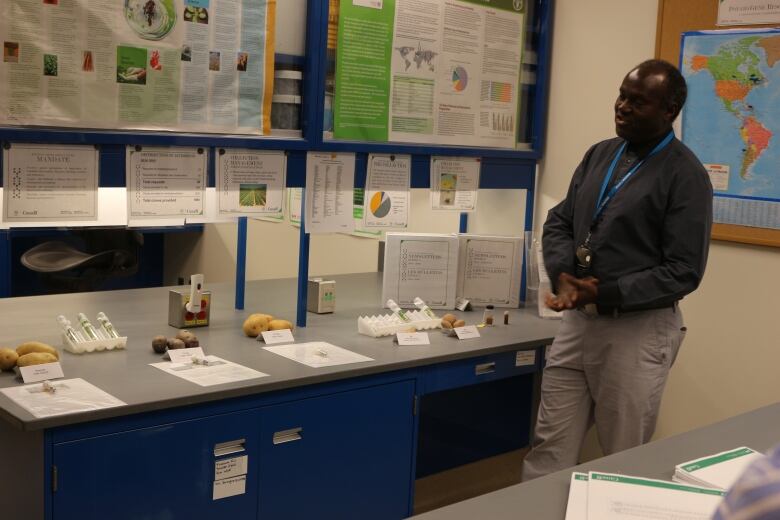 A man wearing a dress shirt and pants stands next to a counter with potatoes on display