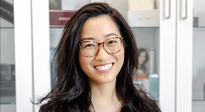 A woman wearing glasses and medical scrubs smiles for the camera 