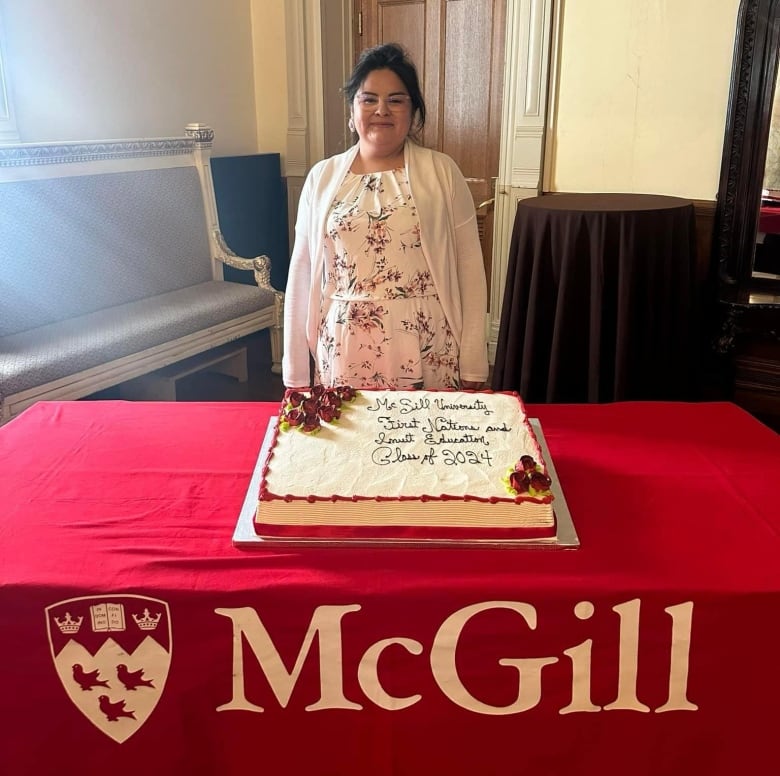 A Cree women stands in front of graduation cake. 