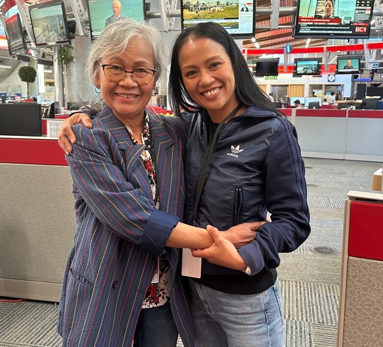 Two women embrace in a newsroom.