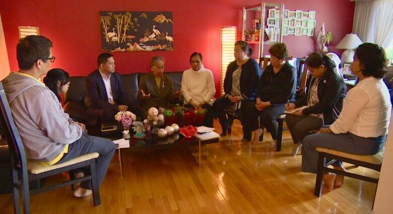 Nine people gathered in a semi-circle as they meet in a living room.