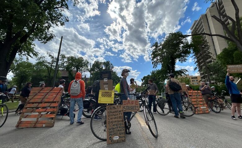 People standing on a street, many besides bikes. Some are holding signs.