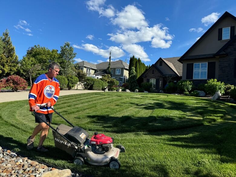 A man mows a lawn wearing an Edmonton Oilers jersey.