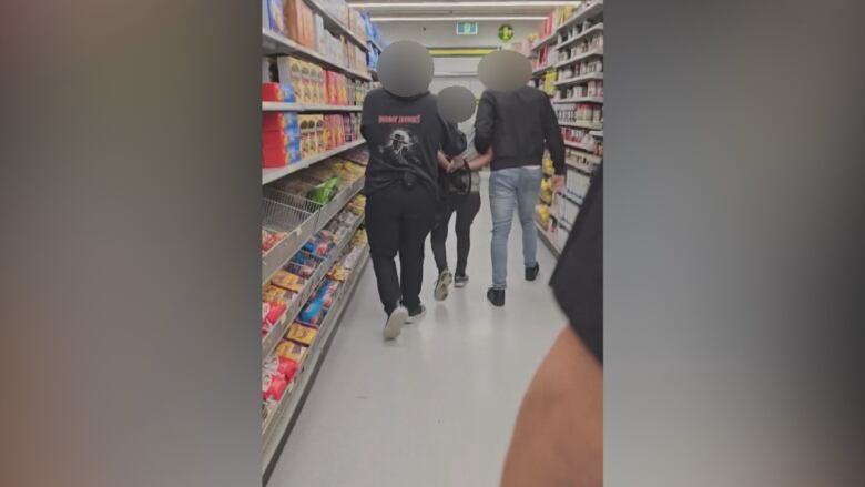 Two people with their faces blurred are seen walking and holding onto another person.