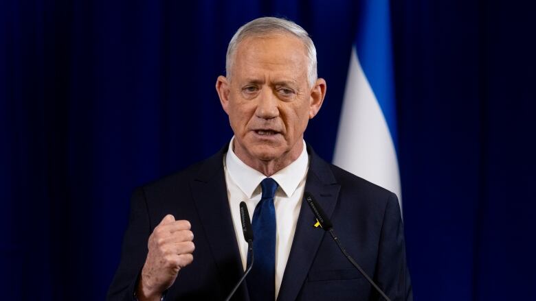 A person gestures while speaking into a microphone at a lectern.