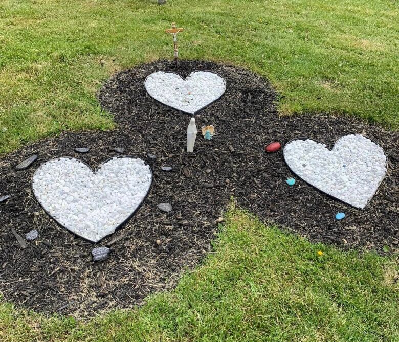 Grass with three circles of dark earth with a heart made of little white rocks in each circle.