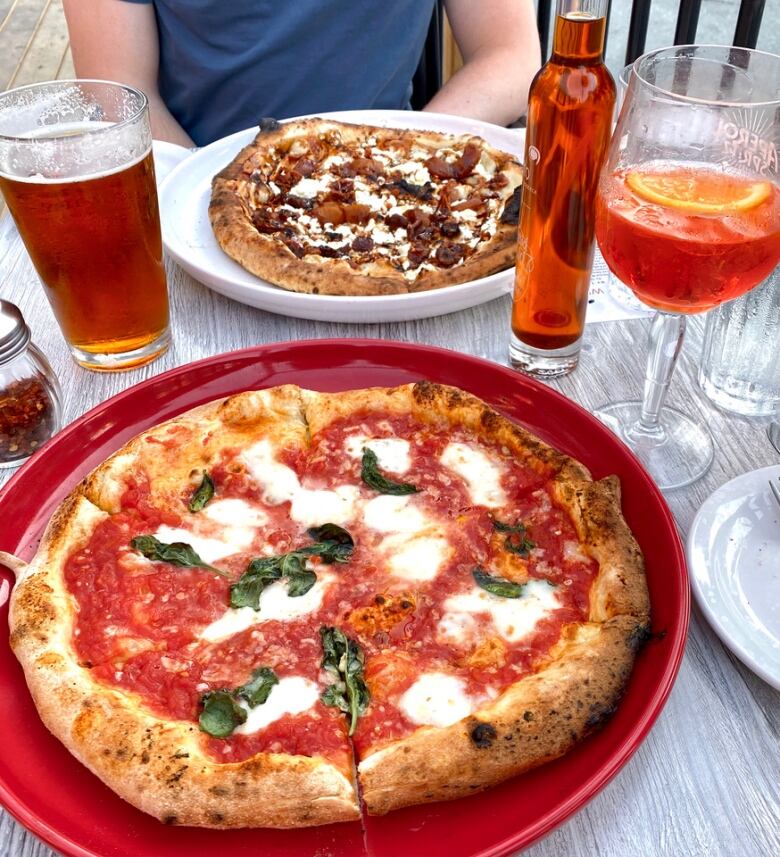 Two pizzas on a table with drinks. 