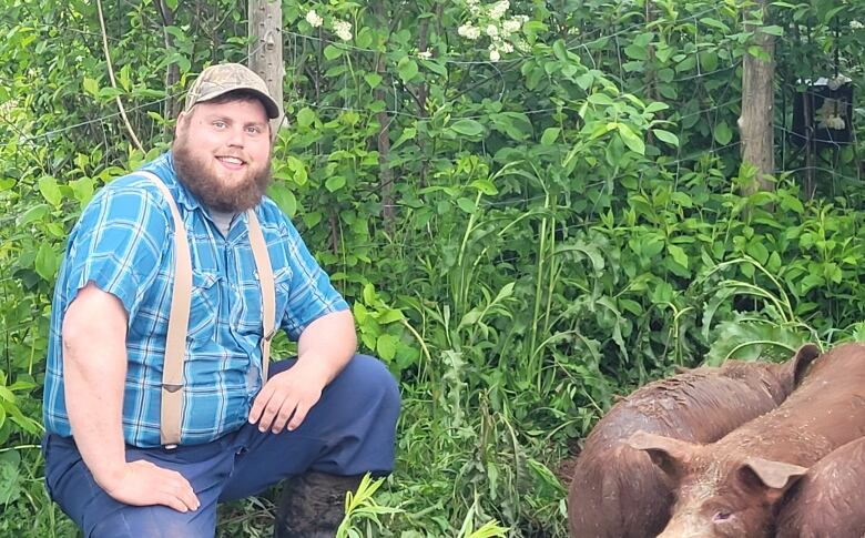 Travis Cummiskey squats next to a fence and several pigs.