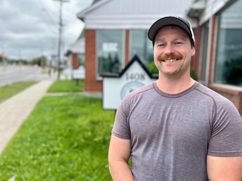 A man smiles into the camera, standing in front of his business