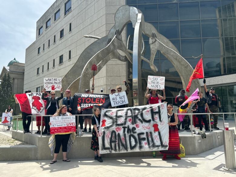 A group of people holding signs, some reading 'search the landfill.'