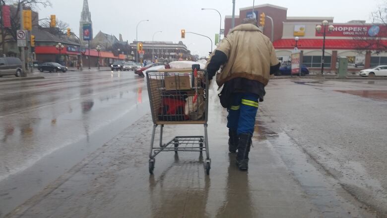 A man walks through a rainy street, pulling a shopping cart