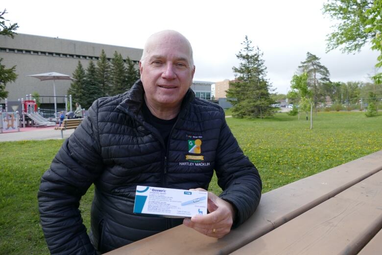 Man sits at picnic table and holds a white box with Ozempic label