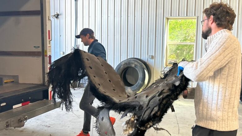 Two men can be seen loading metallic structures on to a truck 