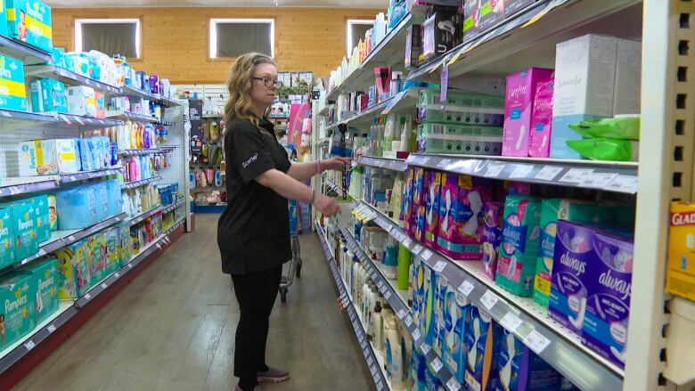 A woman in her late 30s or early 40s stands next to drug store shelving.