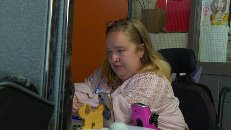 A 20-something woman in a wheelchair looks at a computer monitor