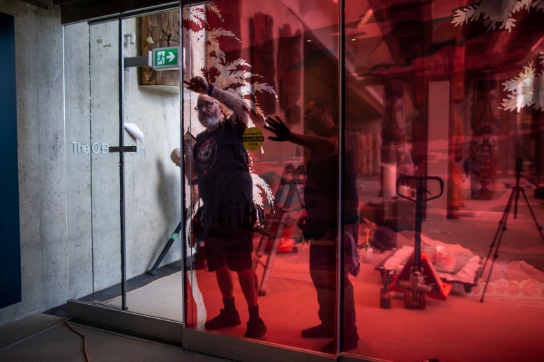 Two men work on a glass wall that is stained with red in a museum.