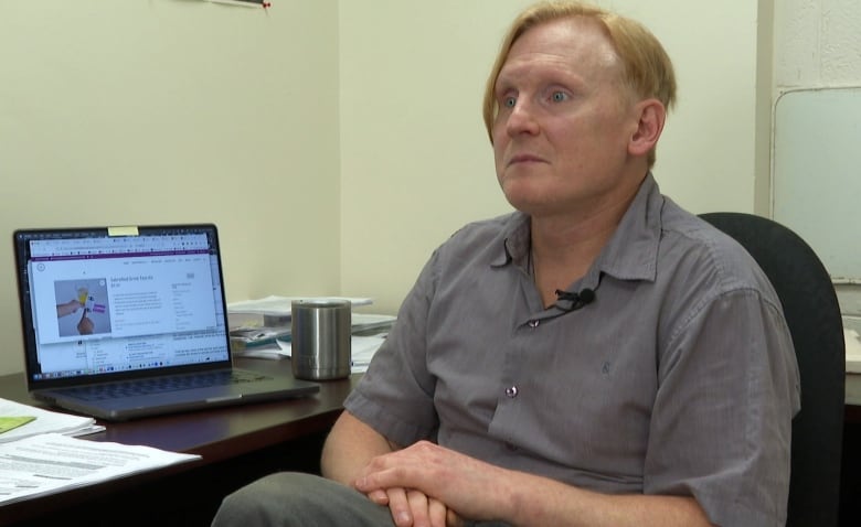 Man sits with his back to a desk with a laptop open displaying a drink test kit. 