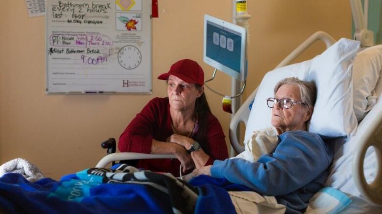 An elderly woman in a hospital bed and a middle-aged woman sitting beside her. They are both looking out a window out of the frame.