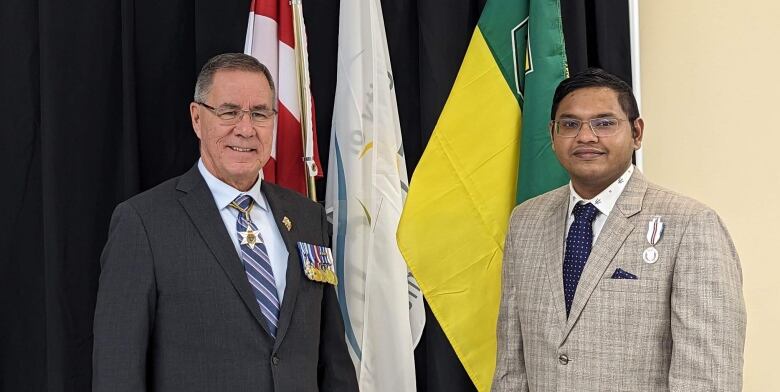 Two men stand in front a Saskatchewan flag.