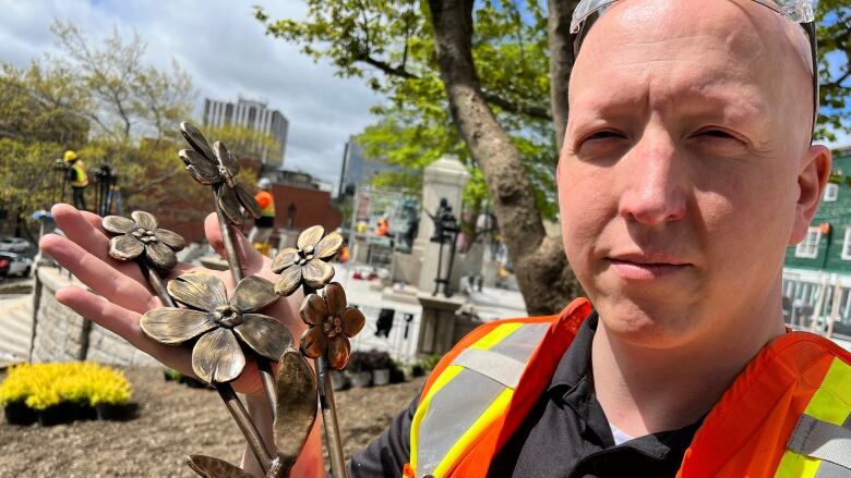 a man holds a bronze flowers, standing in front of a war memorial.