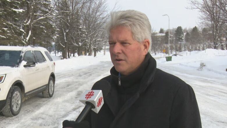 Grey-haired man speaks into a microphone.