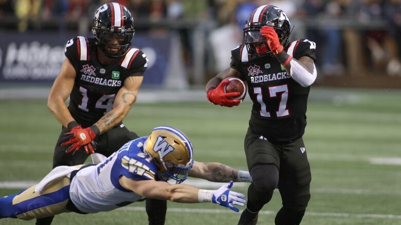 Football player in white uniform dives for the ankles of a ball carrier in a black uniform.