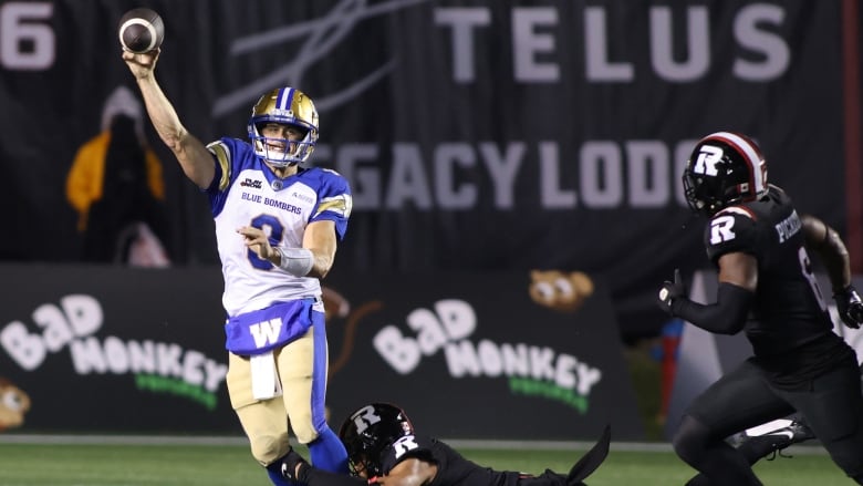 A football player in black dives at the ankles of a quarterback in white, just as he releases the football.