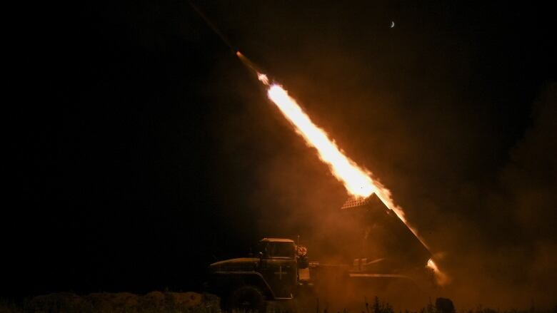 A large burst of fire is shown from a vehicle in a nighttime photo.