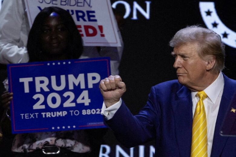 Trump pumping fist with Trump 2024 signs in the background