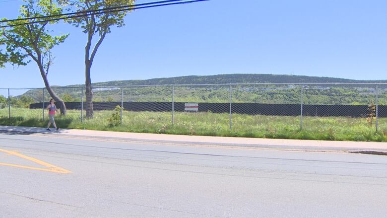 A woman walks past a large fenced-in vacant area.