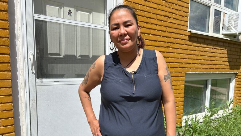 A woman stands outside near her front door with her left hand on her hip. 