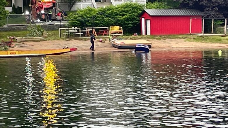 Image of a police officer standing on the shore while an emergency vehicle pulls a car out of a lake.