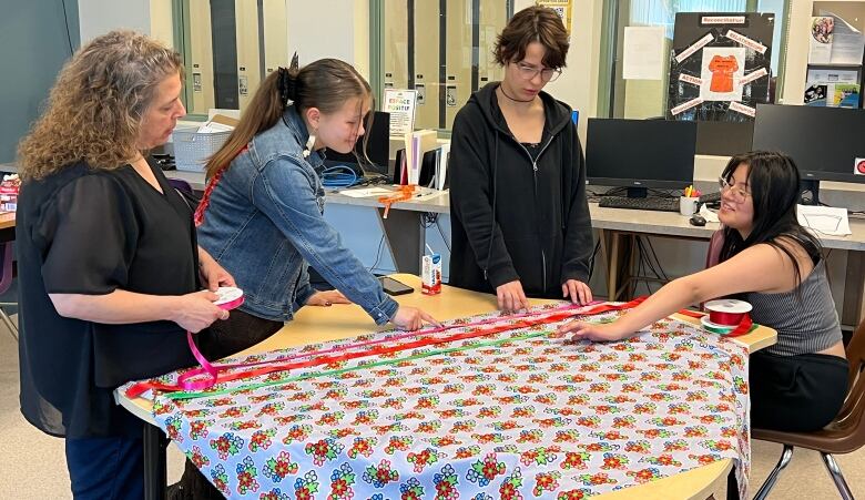 Four people overlook colourful fabric laid out on a table.