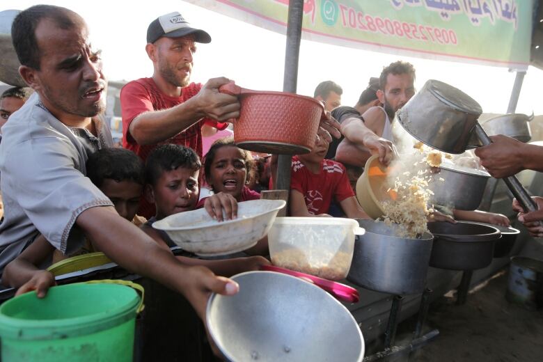 Hungry Palestinians jostle for food with bowls in their hands.