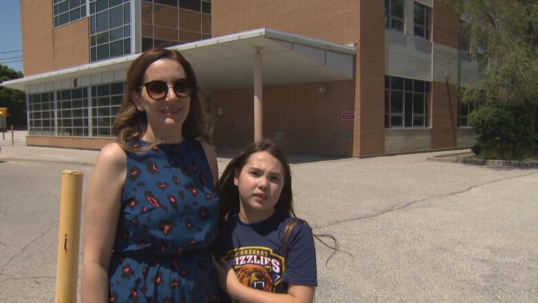 A woman and her daughter stand outside of a school.