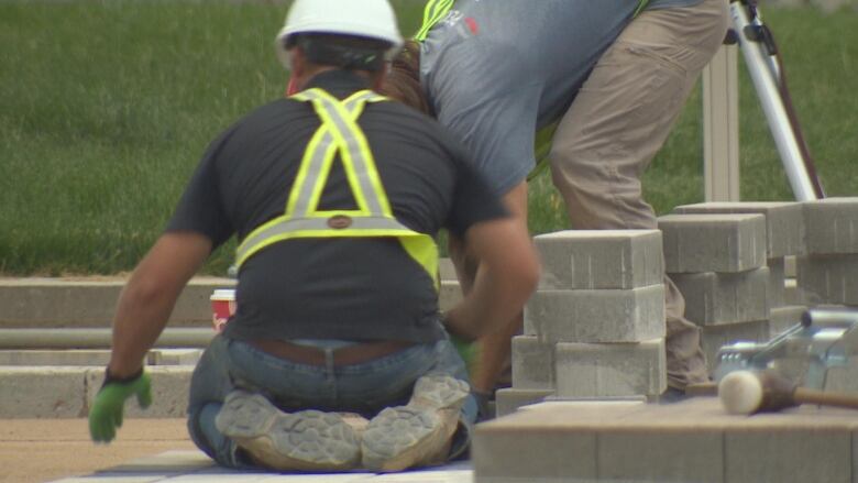 Two construction workers laying paver stones on a walk way.